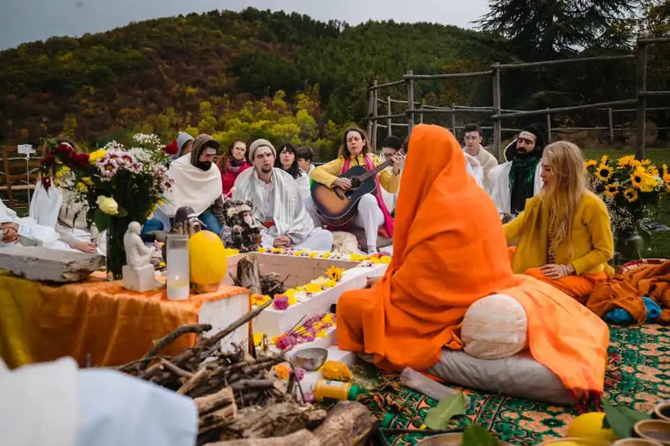 A group of people gathered on blankets for an outdoor gathering with musical instruments and colorful clothing.