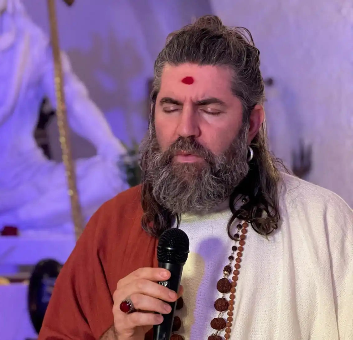 Man with beard and red mark holding microphone.