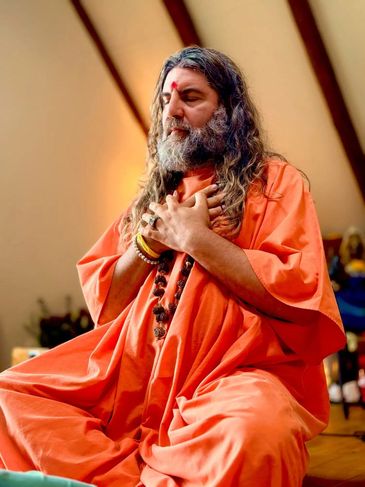 A man wearing a flowing orange robe with long, wavy hair and a beard.