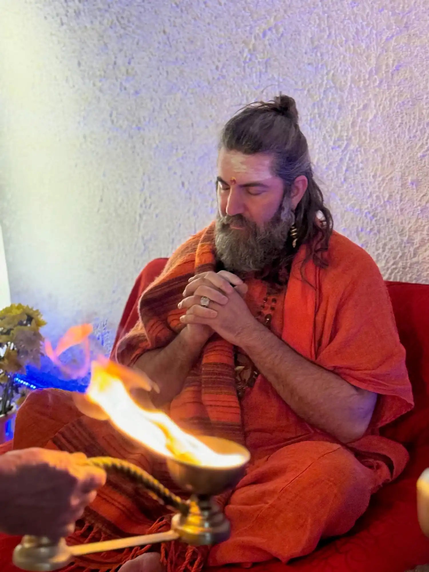 Man in orange robes meditating by fire.