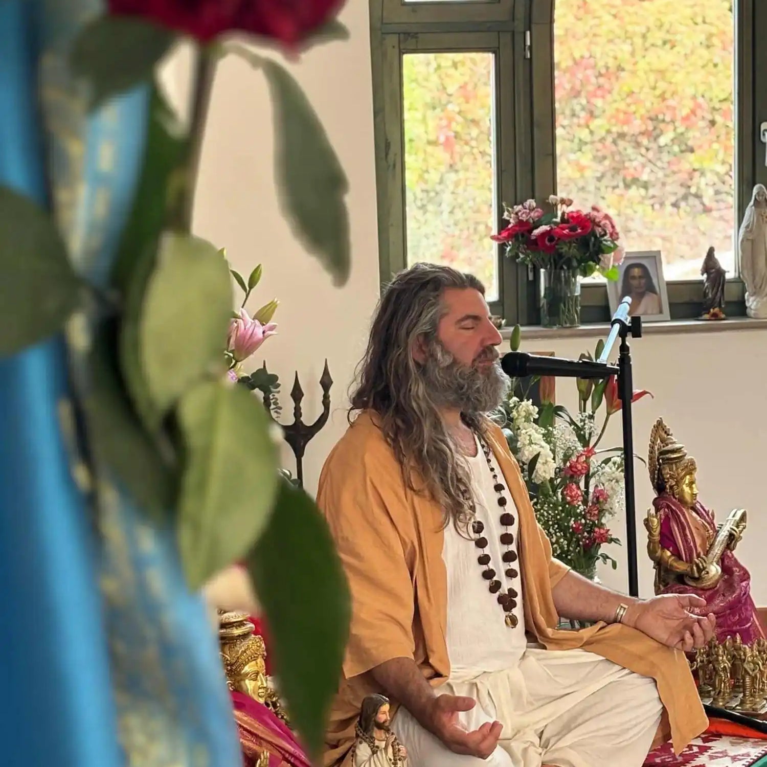 A spiritual teacher with long hair and a beard, meditating in traditional clothing.